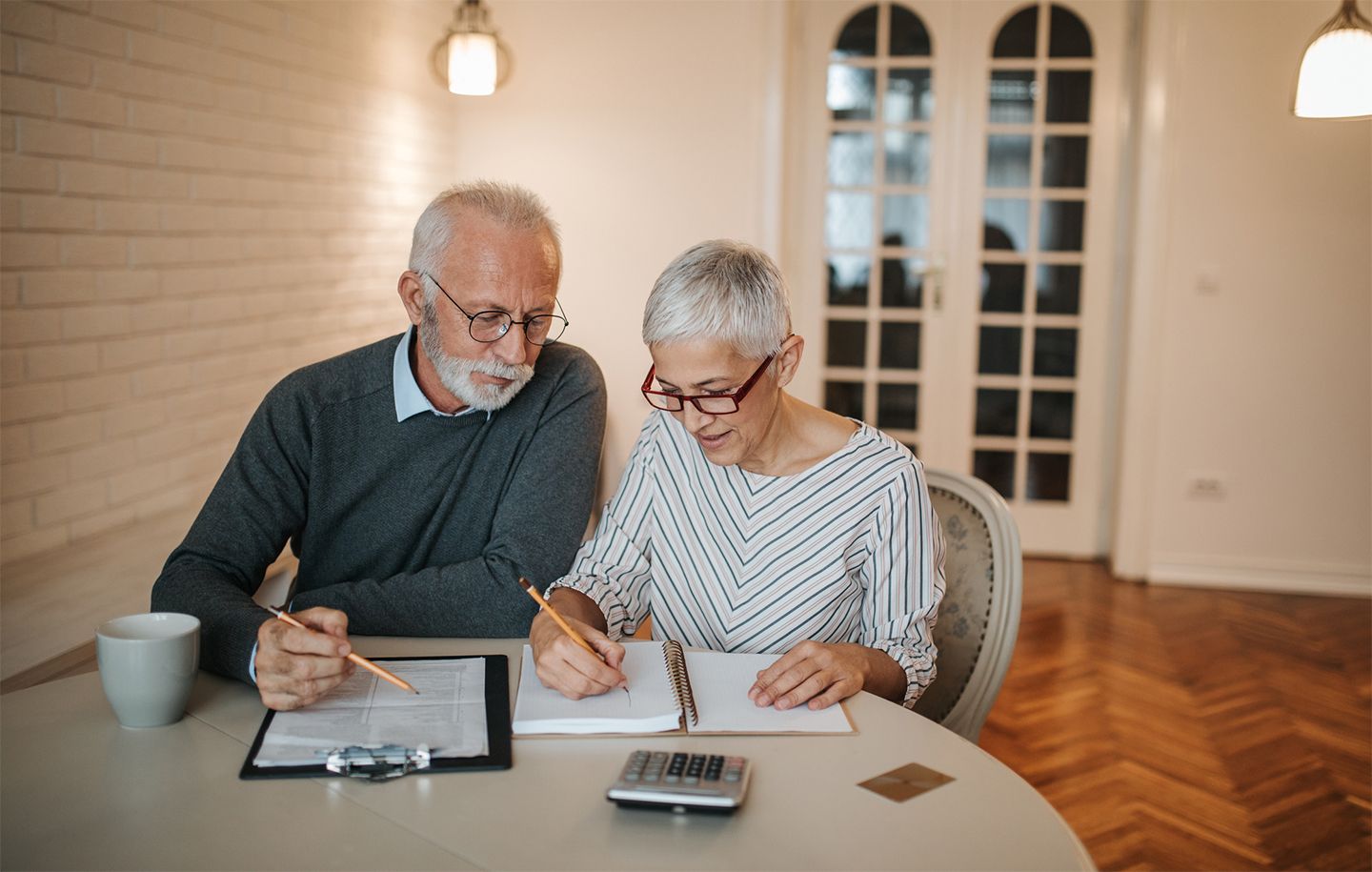 Two senior citizens sitting at a kitchen table and going over some paperwork with a calculator on the tabletop